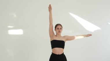 Siyah elbiseli genç kadın beyaz arka planda çağdaş dans ediyor..