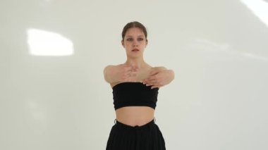 Siyah elbiseli genç kadın beyaz arka planda çağdaş dans ediyor..