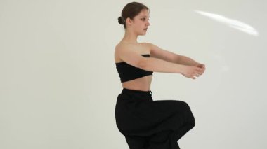 Siyah elbiseli genç kadın beyaz arka planda çağdaş dans ediyor..