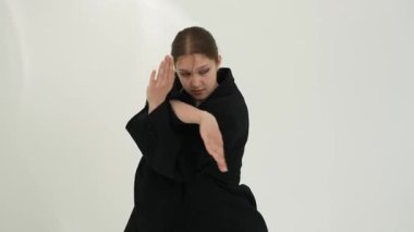 Siyah elbiseli genç kadın beyaz arka planda çağdaş dans ediyor..