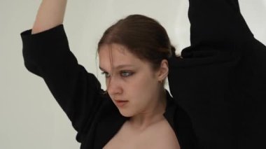 Siyah elbiseli genç kadın beyaz arka planda çağdaş dans ediyor..