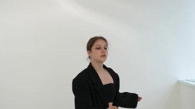 Siyah elbiseli genç kadın beyaz arka planda çağdaş dans ediyor..