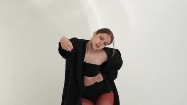 Siyah elbiseli genç kadın beyaz arka planda çağdaş dans ediyor..