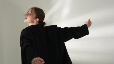 Siyah elbiseli genç kadın beyaz arka planda çağdaş dans ediyor..