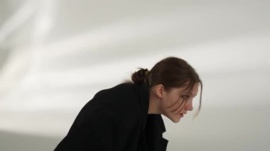 Siyah elbiseli genç kadın beyaz arka planda çağdaş dans ediyor..