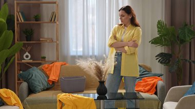 Günlük yaşam tarzı konsepti. Genç bir kadın hafta sonları evde vakit geçiriyor. Ev temizliği yapıyor. Oturma odasında dağınık çamaşırlara bakıyor..