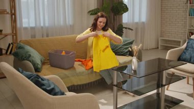 Günlük yaşam tarzı konsepti. Genç bir kadın evde vakit geçiriyor, hafta sonları temizlik yapıyor, kadın oturma odasında kanepede oturuyor ve temiz çamaşırları sepete koyuyor..