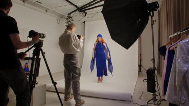 Günlük yaşam tarzı konsepti. Profesyonel bir stüdyoda fotoğrafçı ve asistanlarla fotoğraf çekimine katılan süslü kıyafetli genç bir kadın model kameraya poz veriyor, çekimi bitiriyor..