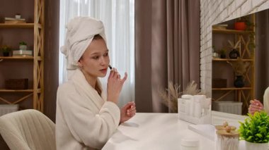 Bir kadın rahat bir evde oturuyor, cilt bakımı için yüz silindiri kullanıyor..