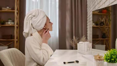 Cilt bakımını yapan bir kadın makyaj masasında otururken kafasına havlu geçirir..