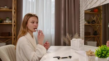 Cüppeli bir kadın, gösterişli bir banyoda aynalı bir şekilde otururken dudak kremi sürüyor..