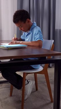 Günlük yaşam tarzı konsepti. Genç Afrikalı Amerikalı çocuk evde vakit geçiriyor, çocuk oyuncu masasında bilgisayarla aydınlık odada oturuyor ve oyun oynuyor, ifade kazanıyor. Dikey video