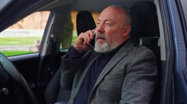 Direksiyon başında akıllı telefondan konuşan yaşlı bir adam. Görüntü odaklanmayı ve bağımsızlığı iletirken, aynı zamanda işe normal bir ortamda gidip geliyor..