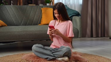 Neşeli bir genç kız yerde oturup gezici bir oyunun tadını çıkarıyor. Rahatlamış ve oyuna dalmış görünüyor..