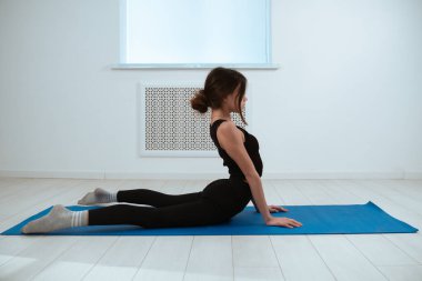 Siyah egzersiz kıyafeti giymiş bir kadın, mavi bir paspasın üzerinde, spor salonuna ve dayanıklılığa odaklanmış, tahta bir poz veriyor..