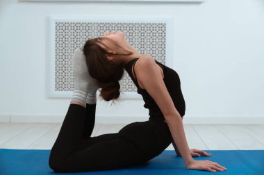 Siyah egzersiz kıyafeti giymiş bir kadın, mavi bir paspasın üzerinde, spor salonuna ve dayanıklılığa odaklanmış, tahta bir poz veriyor..