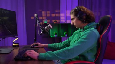 Günlük yaşam tarzı konsepti. Genç yetişkin bir adam evde vakit geçirir, erkek flamalı oyuncu masasına oturur, neon ışıklı odada bilgisayarla çevrimiçi yayın yapar, oyun kaybeder, sinir bozucu ifade bozulur..