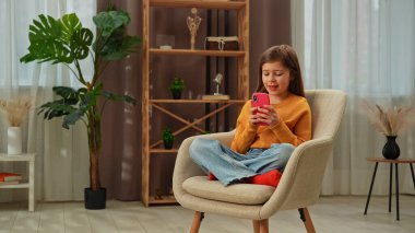 Günlük yaşam tarzı konsepti. Genç kız akşam vaktini evde geçiriyor, kız oturma odasında oturuyor ve akıllı telefondan mesaj atıyor, gülümsüyor..