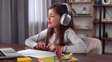 Günlük yaşam tarzı konsepti. Evde okuyan küçük bir kız çocuğu, küçük bir kız, masa başında oturuyor ve internette okul derslerine katılıyor, ödev yapıyor, öğretmenler el kaldırıyor ve soruları cevaplıyor..