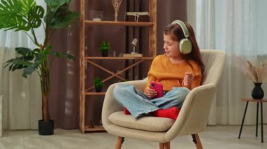 Günlük yaşam tarzı konsepti. Genç kız akşam vaktini evde geçirir, kız oturma odasında oturur ve kulaklıkla müzik dinler, şarkı söyler. Yavaş çekim.