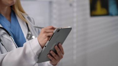 Bir sağlık uzmanı, klinik ortamda veri girişi ve hasta yönetimi için bir tablet kullanır. Kapat.