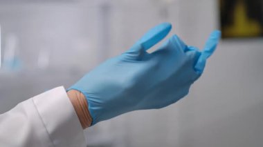 Laboratuvar ortamında mavi lateks eldiven takan bir kişi, güvenlik ve hijyen protokollerine vurgu yapıyor. Yaklaşın, ağır çekim.