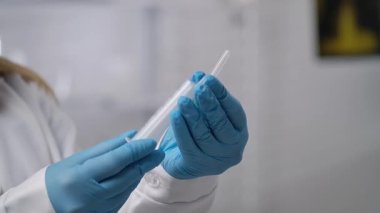 Mavi eldiven giyen bir tıp uzmanının elinde şırınga var. İğne ya da aşıya hazır. Yavaş çekim