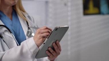 Klinik ortamında dijital tablet kullanan önlüklü ve laboratuvar önlüklü bir sağlık uzmanı. Kapat.