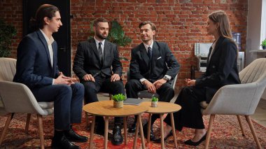 İş kıyafetli dört kişi, tuğla duvarlı ve modern dekorlu şık bir ofiste buluşuyor..