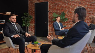 Bir grup profesyonel, modern ofis ortamında tuğladan bir arka planı olan bir iş görüşmesinde yer aldılar..