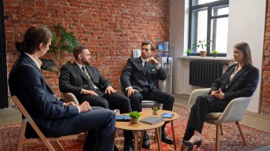 Dört iş adamı, duvarları ve bitkileri olan şık bir ofiste toplanıp stratejileri tartışırlar..