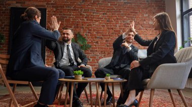 Takım elbiseli iş adamlarından oluşan bir ekip modern ofis ortamında, takım çalışmasını ve başarıyı simgeleyen mutlu bir beşlik çakışması..