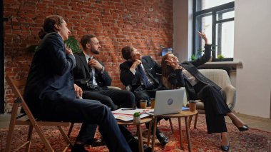 Takım elbiseli dört profesyonel şık bir ofiste oturup selfie çekiyorlar, takım çalışması ve dostluk gösteriyorlar..