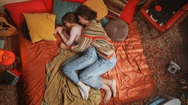 Sıcak renklerle çevrili canlı bir yatakta sarılan bir çift rahatlama ve rahatlama hissi yaratıyor. Üst çekim