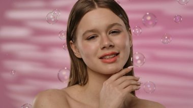 Genç bir kadın, etrafında kabarcıklar uçuşurken neşeyi ifade eder. Yumuşak pembe bir arkaplan üzerine kurulur. Huzurlu bir anın altını çizer..