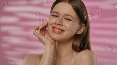 Genç bir kadın, etrafında kabarcıklar uçuşurken neşeyi ifade eder. Yumuşak pembe bir arkaplan üzerine kurulur. Huzurlu bir anın altını çizer..