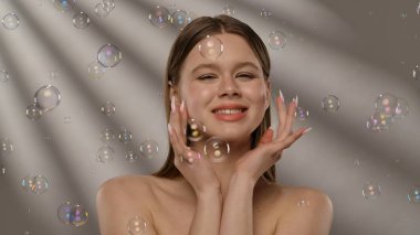 Gülümseyen bir kadın ışıldayan sabun köpükleriyle çevrili, neşeli ve kaprisli bir sahne yaratıyor..
