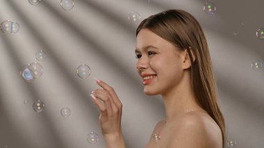 Gülümseyen bir kadın ışıldayan sabun köpükleriyle çevrili, neşeli ve kaprisli bir sahne yaratıyor..