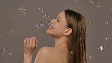 Uzun saçlı bir kadın neşeli bir şekilde renkli baloncuklarla çevrili, tarafsız bir arkaplanda mutlu bir şekilde gülümsüyor..