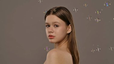 Hafifçe aydınlatılmış arka planı kabarcıklarla çevrili bir kadın. Görüntü bir sakinlik ve güzellik hissi uyandırıyor..