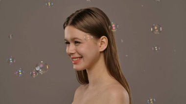 Gülümseyen bir kadın ışıldayan sabun köpükleriyle çevrili, neşeli ve kaprisli bir sahne yaratıyor..