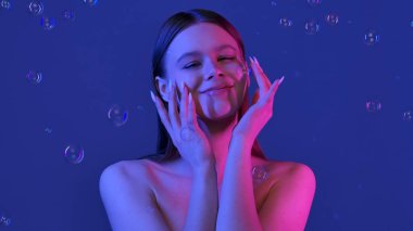 Etrafı baloncuklarla çevrili, yumuşak, mavi bir arka planı olan bir kadın. Görüntü bir sakinlik ve güzellik hissi uyandırıyor..