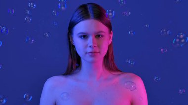 Parlak mavi arka planda köpüklerle çevrili bir kadın. Görüntü bir sakinlik ve güzellik hissi uyandırıyor..