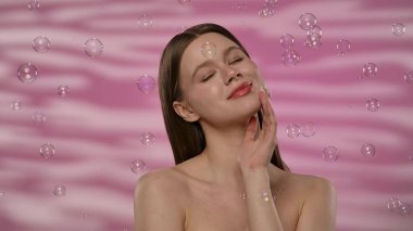 Sabun köpüklerinin pembe arka planda süzülmesi gibi bir kadın neşeyle gülümsüyor, bir neşe ve kapris hissi uyandırıyor. Yavaş çekim