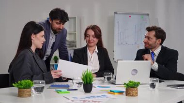 Ofiste bir iş toplantısına katılan dört profesyonel, çizelgelerle stratejiyi tartışıyor..