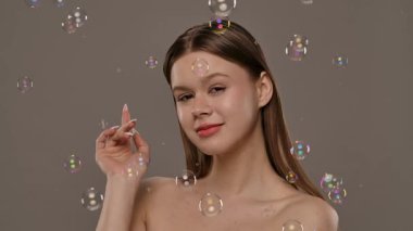 Hafifçe aydınlatılmış arka planı kabarcıklarla çevrili bir kadın. Görüntü bir sakinlik ve güzellik hissi uyandırıyor. Yavaş çekim