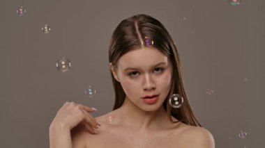 Hafifçe aydınlatılmış arka planı kabarcıklarla çevrili bir kadın. Görüntü bir sakinlik ve güzellik hissi uyandırıyor. Yavaş çekim