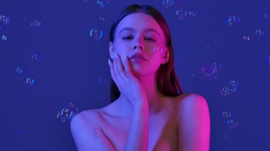 Parlak mavi arka planda köpüklerle çevrili bir kadın. Görüntü bir sakinlik ve güzellik hissi uyandırıyor. Yavaş çekim