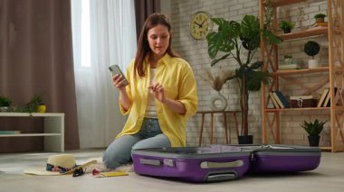 Bir kadın bavulunu topluyor ve akıllı telefonunu kontrol ediyor, muhtemelen seyahate ya da tatile hazırlanıyor..