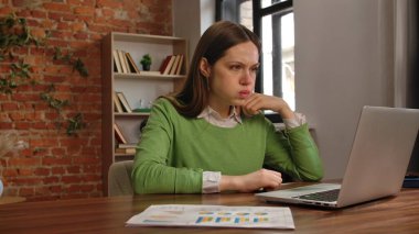 Bir kadın dikkatle dizüstü bilgisayardaki işine odaklanmış. Etrafı çizelgelerle ve duvarlarla çevrili..